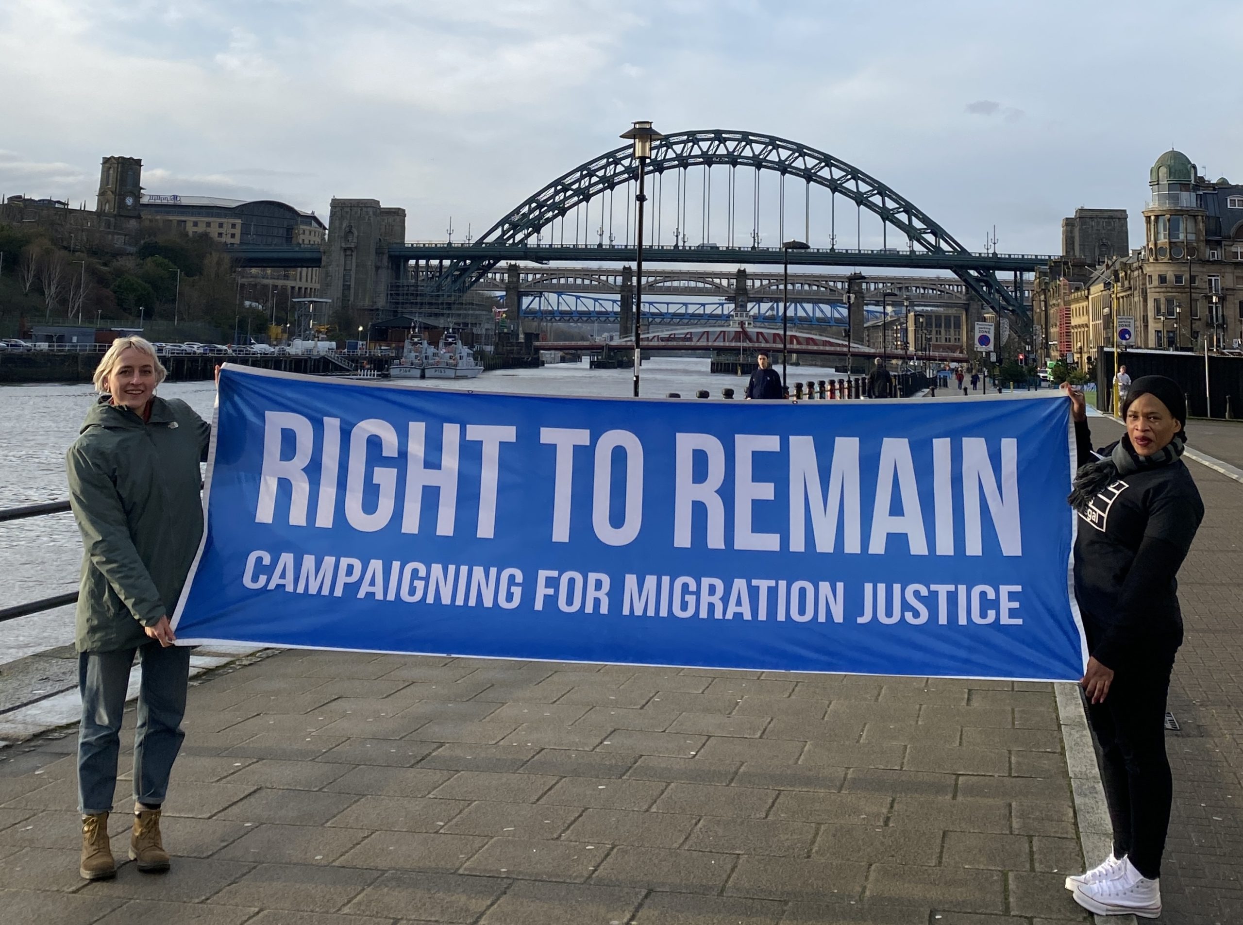 Two Right to Remain staff members holding up a banner that reads 'Right to Remain, campaigning for migration justice'