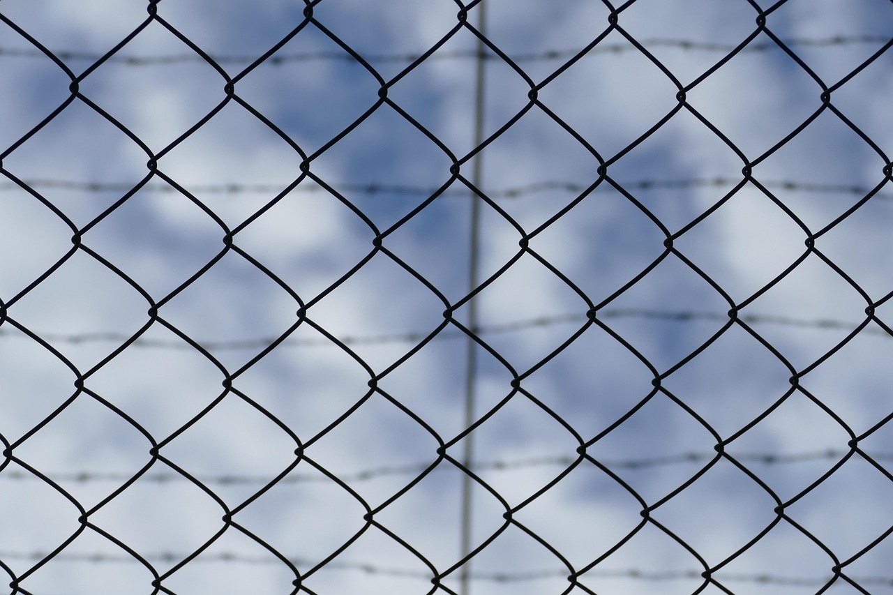 a barbed wire fence against the background of a blue but cloudy sky